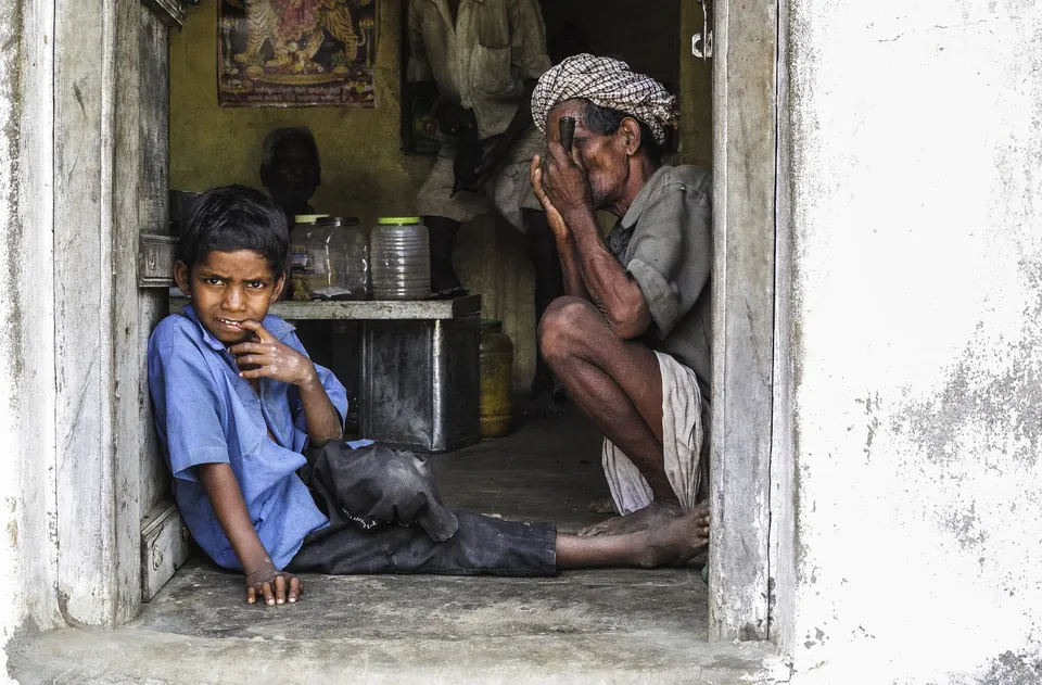 A boy sits in a shop doorway beside an older man in India